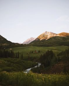 the mountains are covered in green grass and trees, with a stream running between them