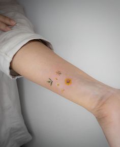 a woman's arm with a small sunflower tattoo on the left side of her arm