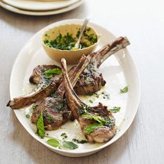 a white plate topped with lamb chops next to a bowl of broccoli