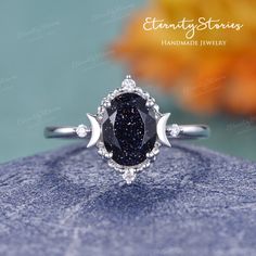 an oval shaped black diamond ring on top of a blue surface with flowers in the background