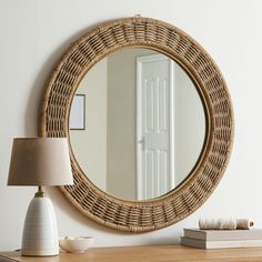 a round mirror sitting on top of a wooden table next to a lamp and book