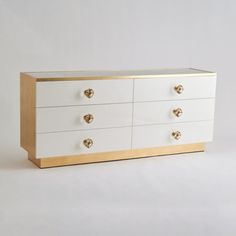 a white dresser with gold handles and drawers on it's sides, against a plain background