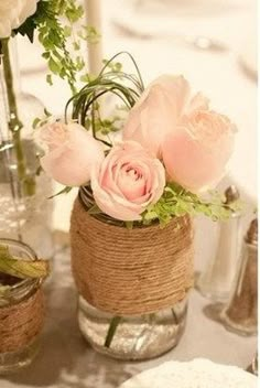 two vases with flowers and twine wrapped around them on top of a table