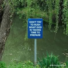 a blue sign sitting in the middle of a lush green forest next to a body of water