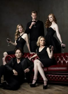 a group of people sitting on top of a red couch with wine glasses in their hands