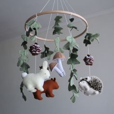 three stuffed animals hanging from a mobile with leaves and acorns on the strings