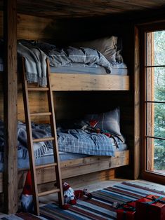 bunk beds with ladders and blankets in a cabin style bedroom, next to a window