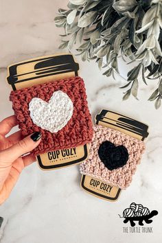 2 crochet coffee sleeves with crochet hearts on top. Cute Crochet Cup Cozy, Crochet Flower Cup Cozy, Mug Pattern Design, Coffee Coozie Crochet Pattern, Valentine Day Crochet Ideas, Crochet Starbucks Cup Cozy, Crochet Patterns Valentines Day, Coffee Cozy Crochet Pattern Free, Crochet Cozy Free Pattern