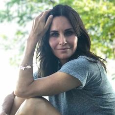 a woman sitting on the ground with her hands behind her head and looking at the camera