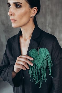 a woman wearing a black shirt holding a green crocheted heart with fringes