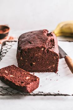 a loaf of chocolate cake sitting on top of a cooling rack next to a banana