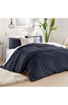 a bed with blue comforter and pillows in a room next to a potted plant