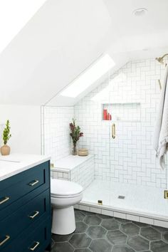 an attic bathroom with white tile and blue cabinetry on the vanity, toilet and shower