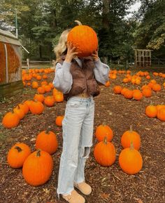 a woman standing in front of a field full of pumpkins with one hand on her head