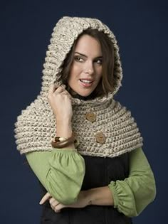 a woman wearing a crocheted hooded sweater and holding her hand on her shoulder