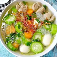 a white bowl filled with soup and vegetables on top of a blue checkered table cloth