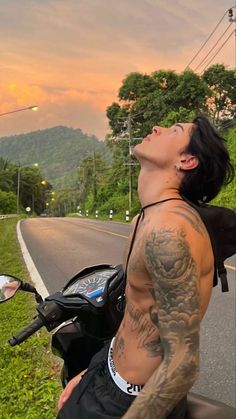 a man with tattoos is looking up at the sky on his motorcycle while he rides down the road