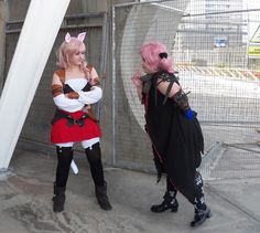 two women dressed in cosplay standing next to each other near a fenced area