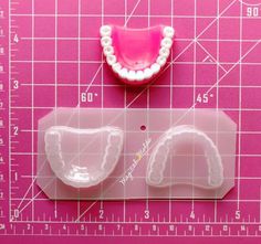 a plastic model of a tooth and gums on a pink background next to a ruler