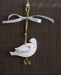 a white bird ornament hanging from a string on a brown background with gold accents