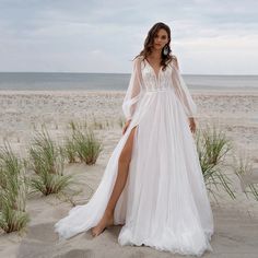 a woman standing on top of a sandy beach wearing a white dress with long sleeves