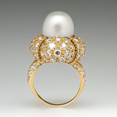 This magnificent cocktail ring is centered with one (1), post set, cultured South Sea pearl. The pearl tops a domed setting is bead set sixty-four (64), bead set, round brilliant cut diamonds. The ring has a split shank design and is accented with seven (7), bead set, round brilliant cut diamonds on each side. The ring measures 21.7mm at the top, rises 18.6mm above the finger, tapering to 2.4mm wide and 1.1mm thick at the base of the shank. The ring is currently size 7. Elegant White Domed Rings, Elegant White Domed Jewelry, Classic Cabochon Pearl Ring For Formal Occasions, Classic Formal Pearl Ring With Cabochon, Classic Cabochon Dome Ring For Wedding, Luxury Pearl Drop Ring For Formal Occasions, Luxury Oval Pearl Ring, Elegant Diamond White Dome Ring For Formal Occasions, Elegant Dome Ring With Cabochon For Wedding