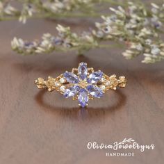 a gold ring with tan and blue stones on it, sitting next to some flowers