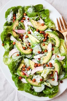 a white plate topped with lettuce and avocado salad next to a fork