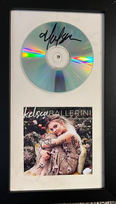 an autographed cd is on display in a black frame with a woman holding a baby