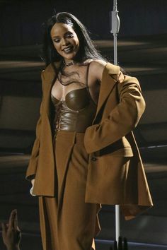 a woman in a brown suit and leather bra is standing next to a metal pole