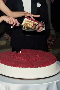 a man and woman cutting into a cake with red raspberries on the bottom