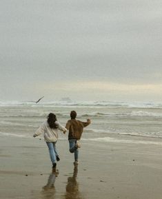 two people running on the beach holding hands