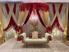 a couch sitting under a chandelier in front of a red and gold backdrop