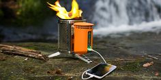 an orange portable stove sitting on top of a rock next to a waterfall with a cell phone hooked up to it