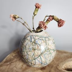 a white vase with pink flowers in it on a wooden table next to a gray wall