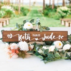 a wooden sign sitting on top of a white table covered in flowers and greenery