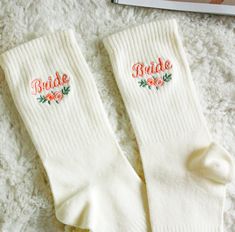 two pairs of white socks with embroidered bride and groom name on them sitting next to an open book