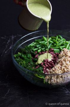 someone pouring dressing onto a bowl of food that includes beans, broccoli and rice