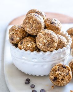 a hand picking up some granola balls from a white bowl with raisins on the side