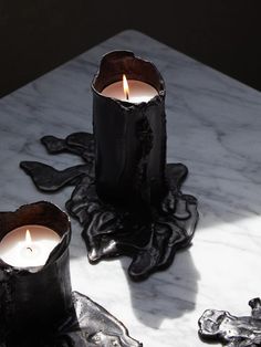 two black candles sitting on top of a white marble table next to another candle holder