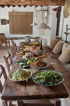 a wooden table topped with lots of plates of food next to a couch covered in pillows