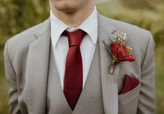 a man in a gray suit with a red tie and flower boutonniere