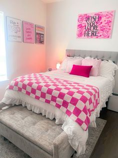 a pink and white checkered bedspread on a bed with a footstool