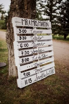 a sign that is sitting in the grass near a tree with writing on it's side