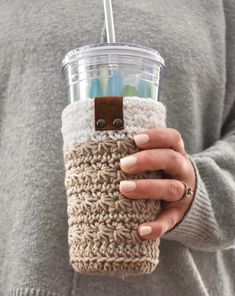 a woman holding a cup with a straw in it and a crocheted sleeve