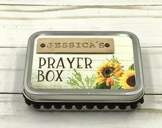 a small metal box with a sunflower design on the front and bottom, sitting on a white wooden surface