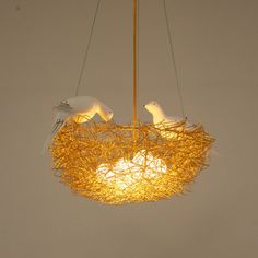 two white birds sitting on top of a bird nest hanging from a ceiling light fixture