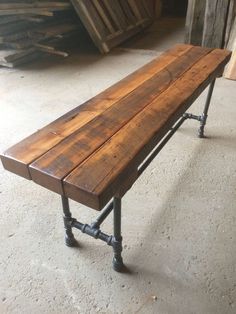 a wooden bench sitting on top of a cement floor next to wood planks and metal pipes