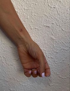 a woman's hand with a tiny tattoo on it, against a white wall