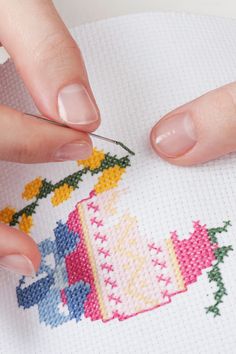 a woman is stitching a cross - stitch pattern on a piece of paper with scissors